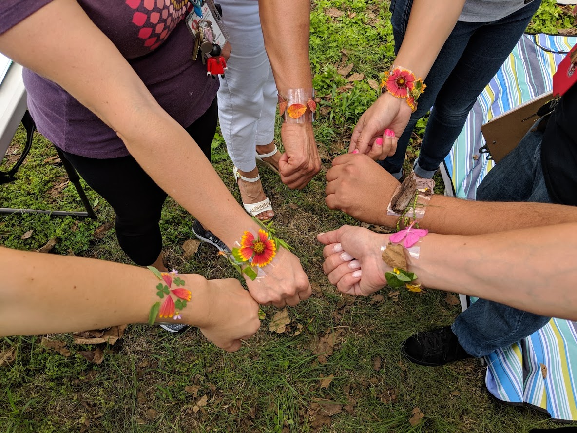 Photo of kids with flower bracelets putting their hands in together.