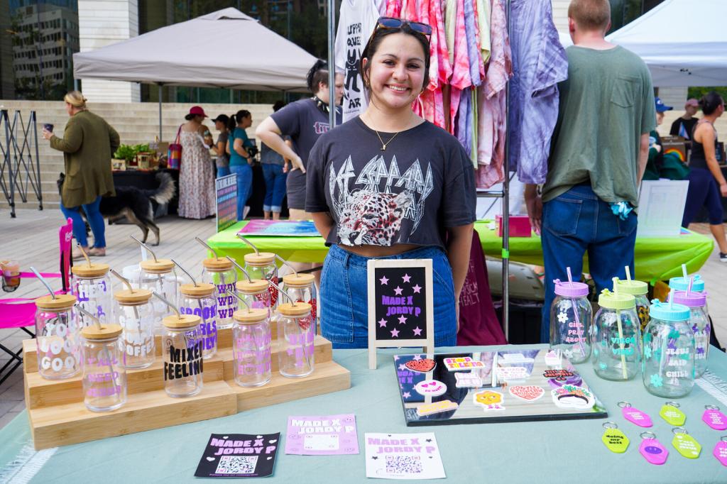 A vendor at The People's Market sells tumblers, stickers, and keychains.