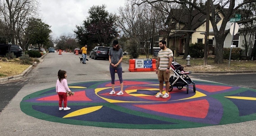 A family walking together in a street with a mandala painted on the pavement