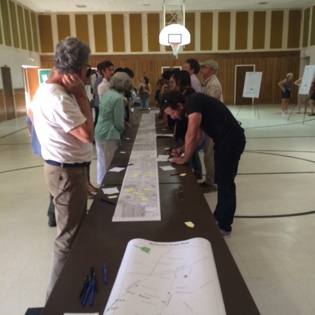 People standing and talking on either side of a long table covered with papers..