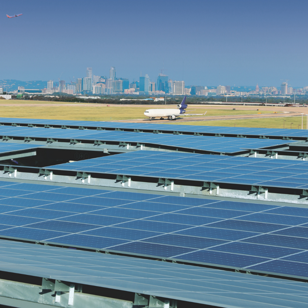 The solar panels on top of the Blue Garage shine brightly in the sun. an Airplane and the Austin downtown skyline are in the background. 