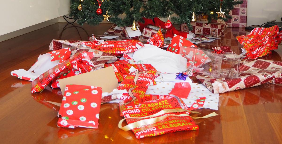 The remnants of used gift wrap and ribbons sit under a tree.