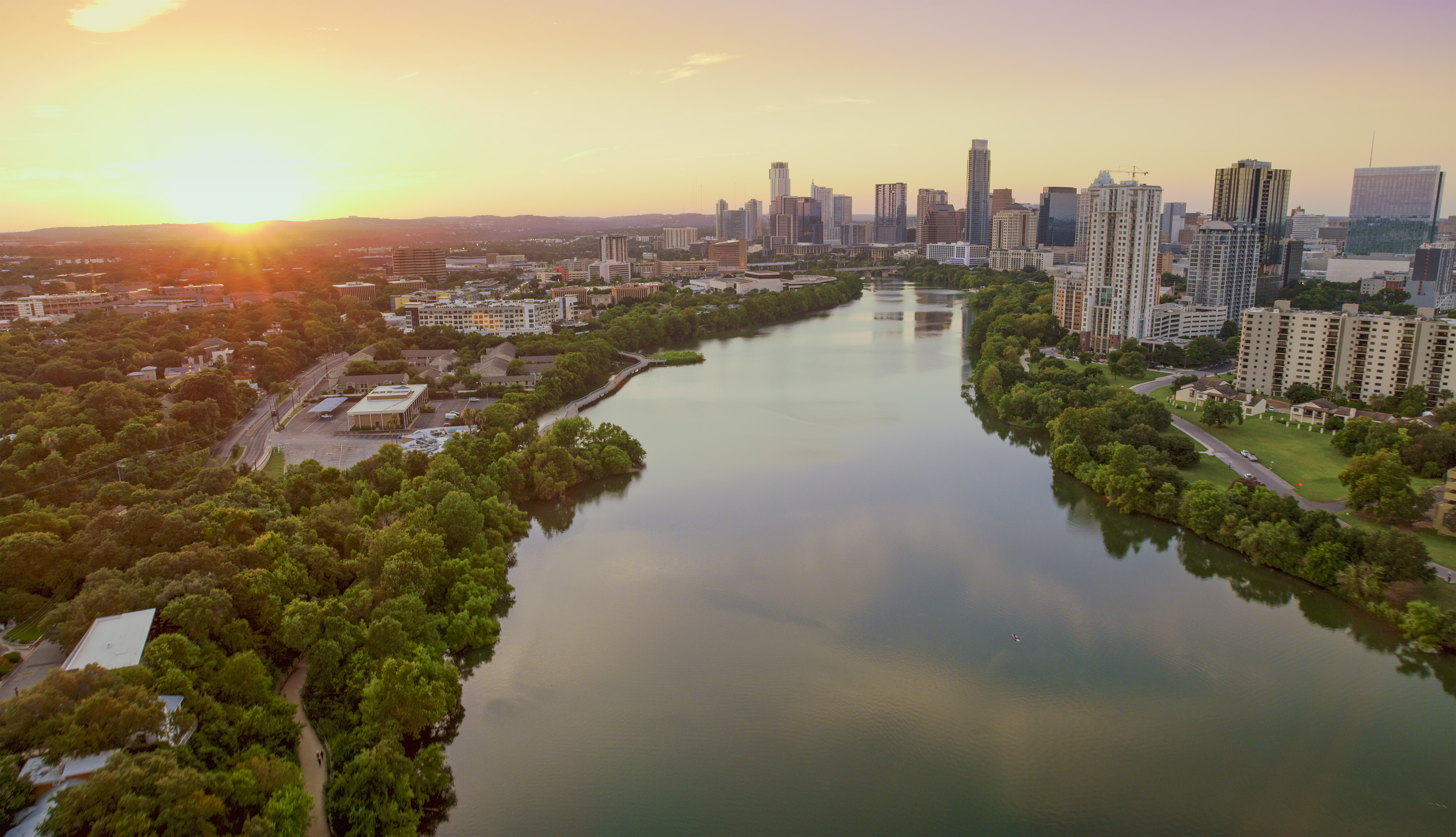 A photo of the sun setting behind Lady Bird Lake and Downtown Austin