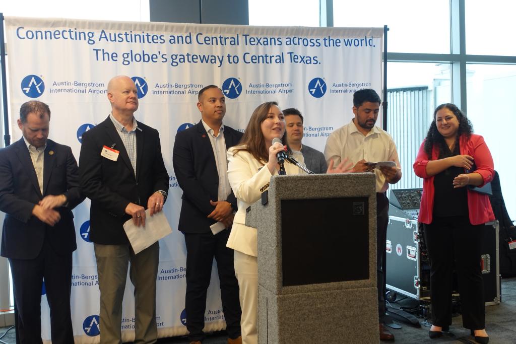 People standing around a podium. One person speaking.