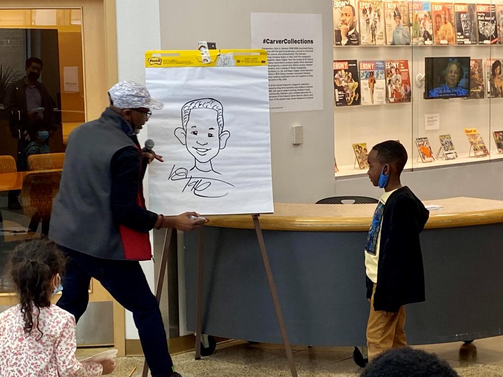 photograph of artist Don Tate drawing a cartoon image of a child in front of an audience of children