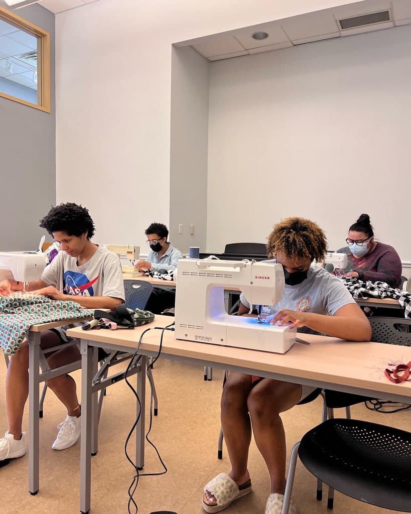 photograph of students in a classroom sitting in front of sewing machines 