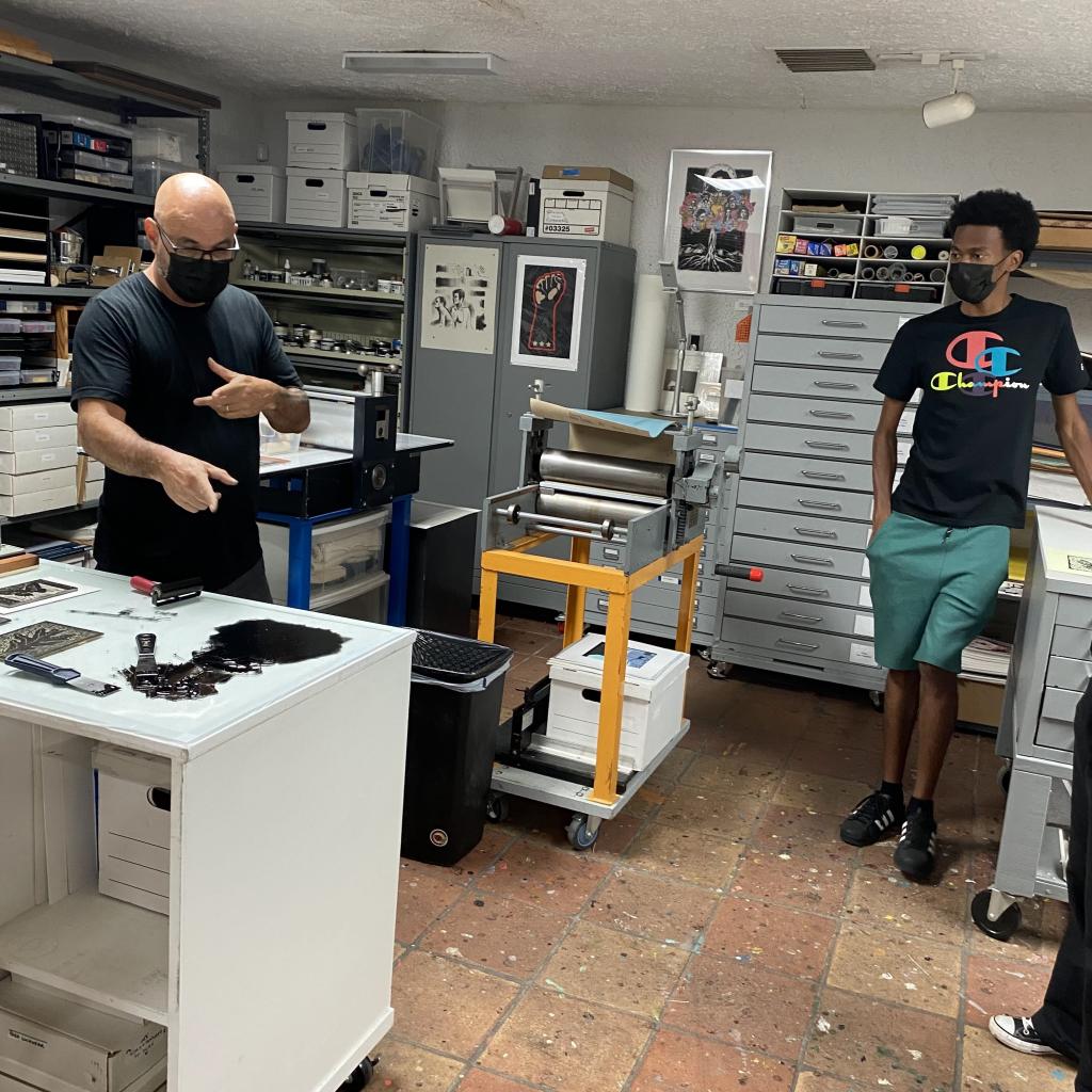 photograph of a print artist demonstrating how to create a print to a student