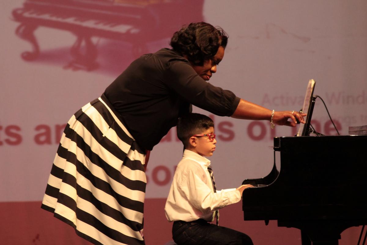 Image: Photo of Piano teacher Daphne McDole beind student playing grand piano turning the pages of the sheet music