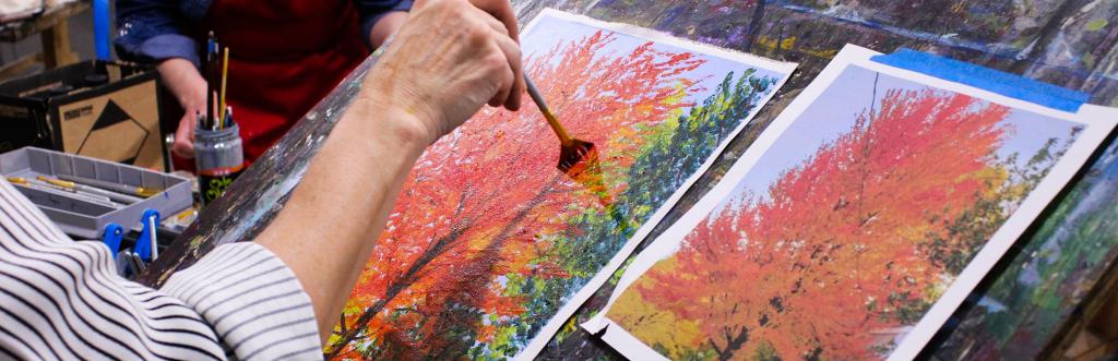 Painting student works on a painting study of an autumn tree from a photograph of the same.
