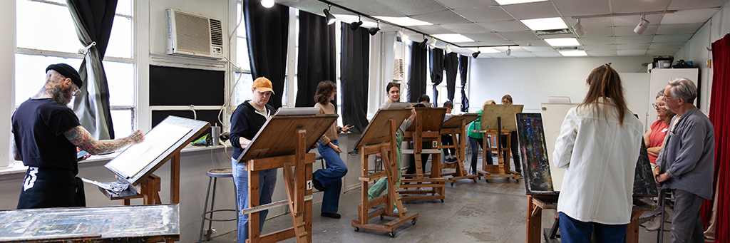A classroom filled with people working on drawings and paintings on easels