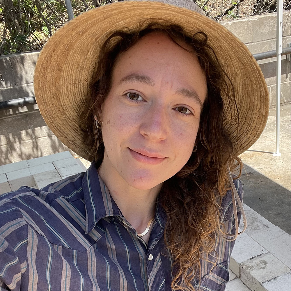A photographic portrait of a person who is wearing a straw hat and smiling at the viewer