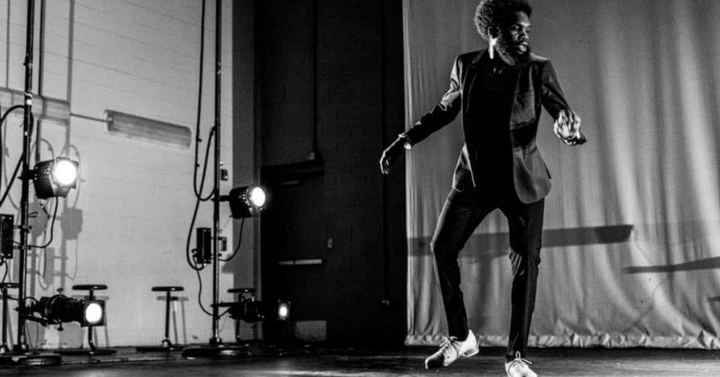 A black and white image of a tap dancer rehearsing on stage.