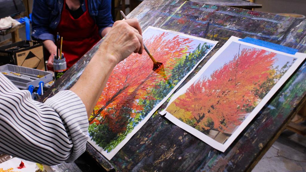 Painting student works on a painting study of an autumn tree from a photograph of the same.