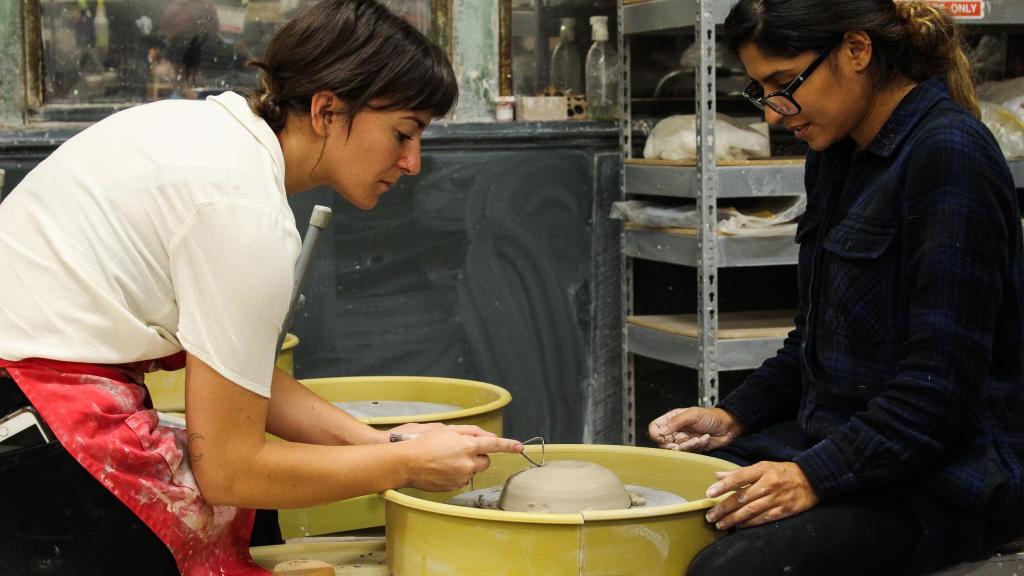 Ceramic arts instructor assists student with wheel throwing exercise