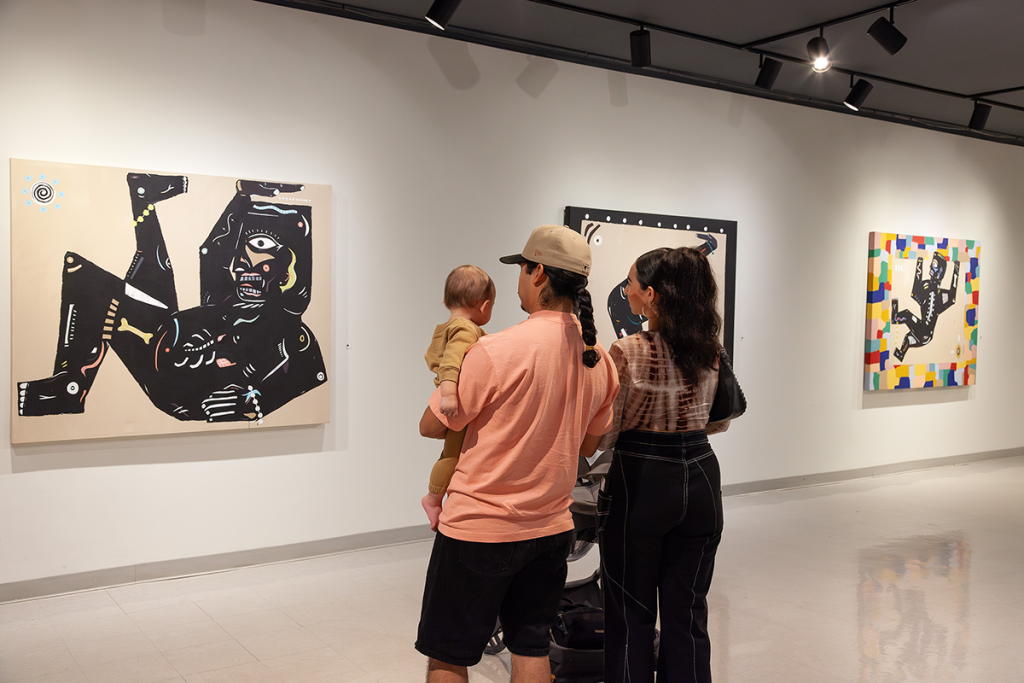 Two people and a child look at artwork on a gallery wall 