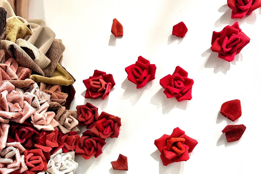 An installation of flowers made from fabric. Grouped together on one portion of a wall and slowly creeping across the wall and spacing themselves apart.