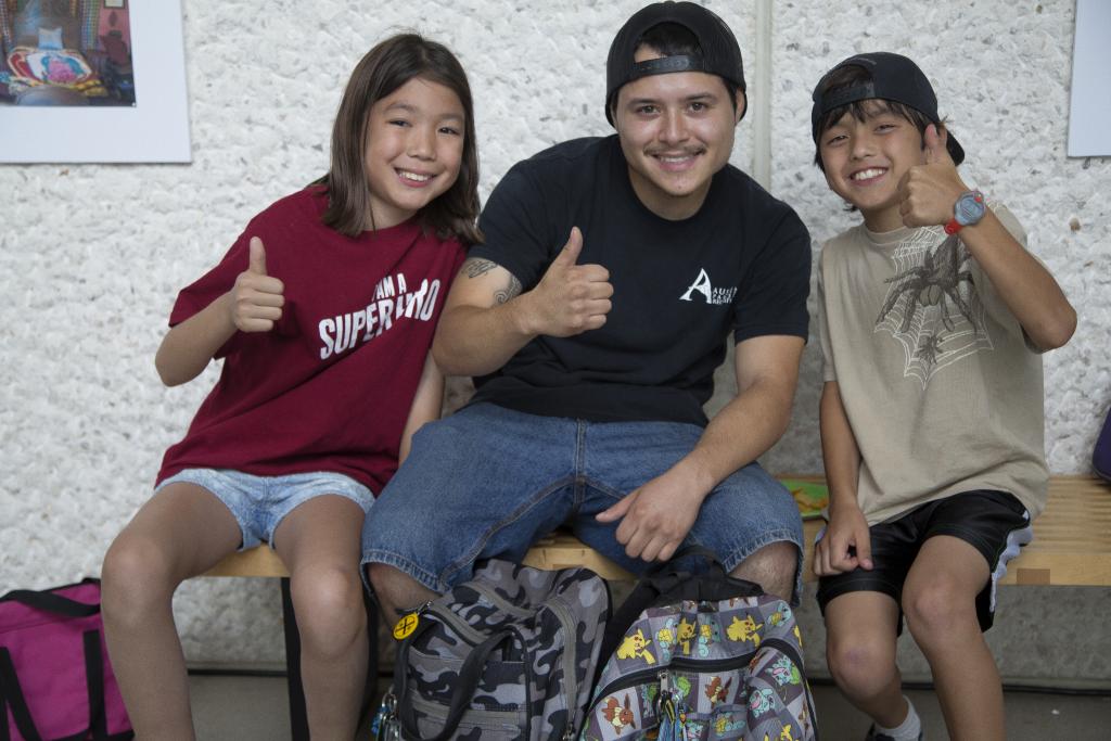 Students of the Cosecha summer camp sit with an instructor on a bench inside the Community Gallery