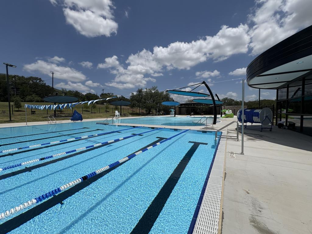 Photo of completed Givens Aquatic Facility overlooking the lap pool and tot pool, with shade structures and alligator water feature. 