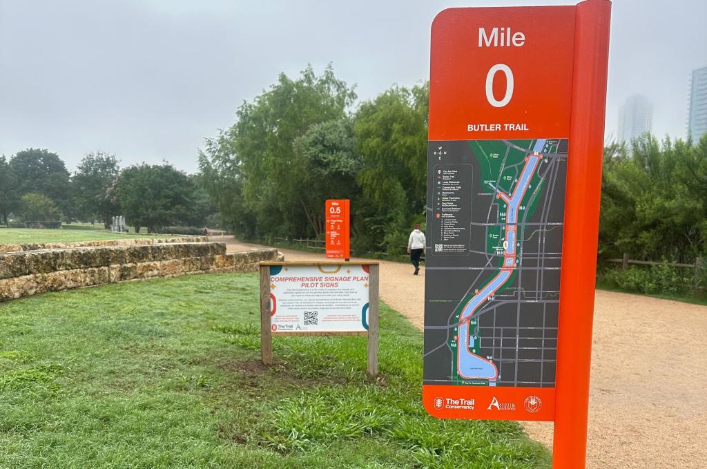 Examples of signs posted on the Trail at Auditorium Shores. Closest sign shows 0 mile marker for Butler Trail with map showing trail route; sign in background shows 0.5 mile.