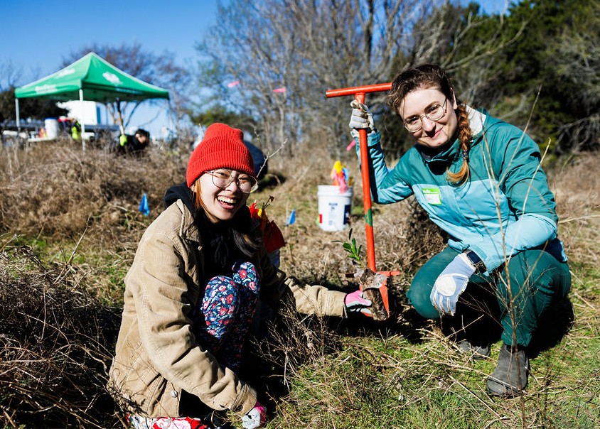 Two smiling volunteers plant a sapling