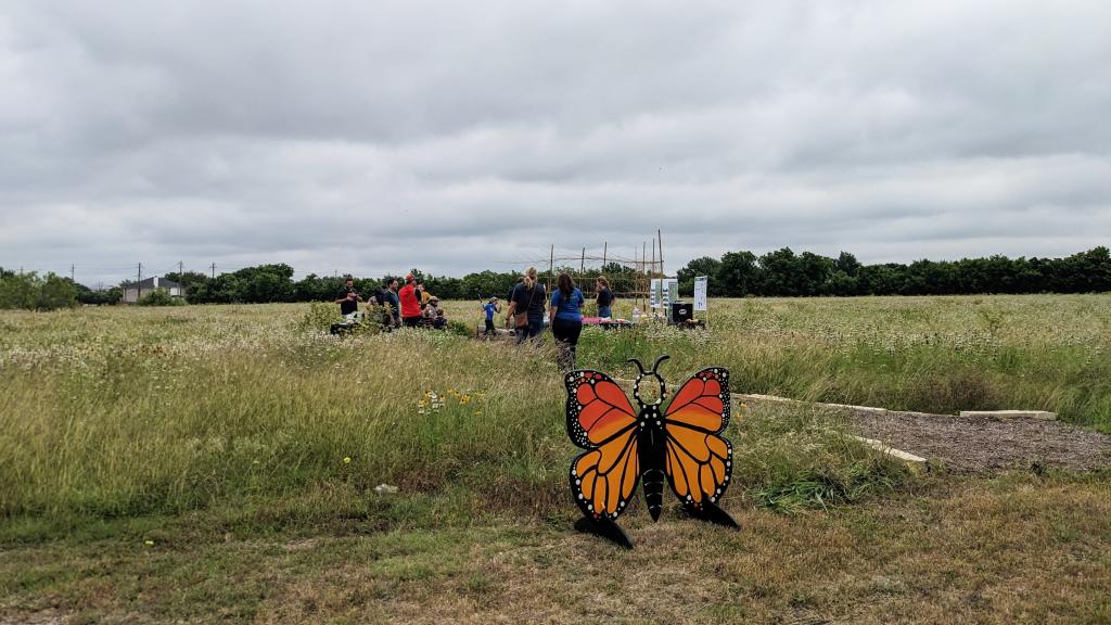 Image of Grand Meadow park with wildflowers and butterfly cutout and people in the meadow