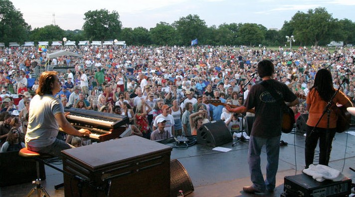 "musicians on stage playing music to a large audience in a park"