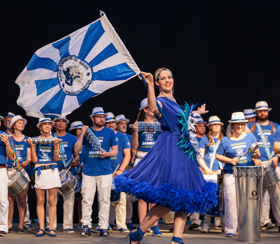 A photograph of a Samba group in blue on a stage