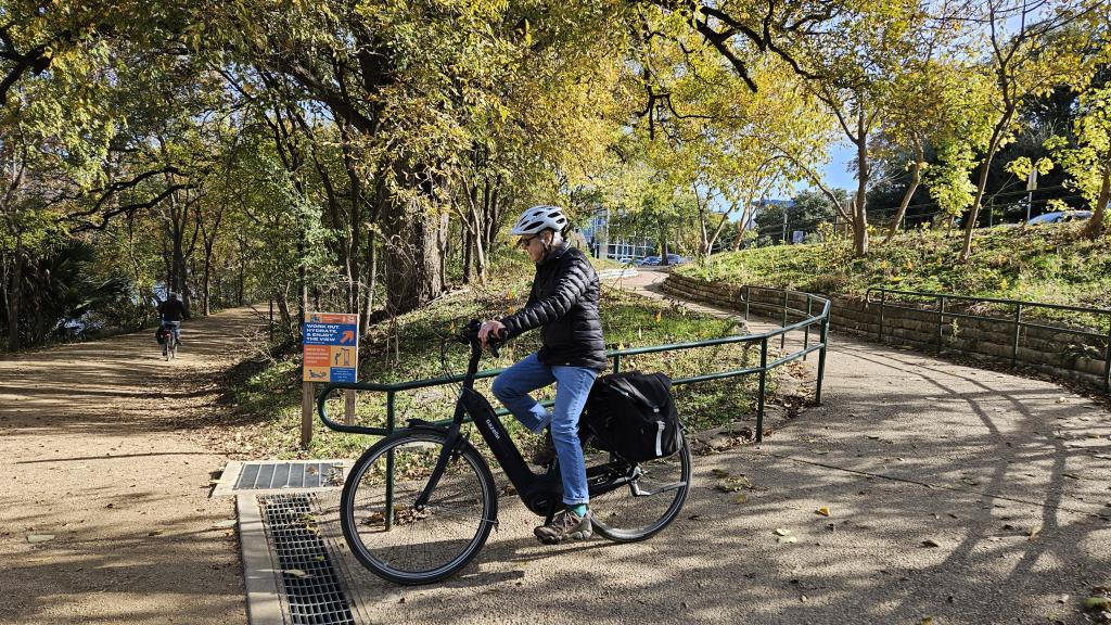 Bike rider rounding the curve on the Ann and Roy Butler Hike and Bike Trail with trees in the background