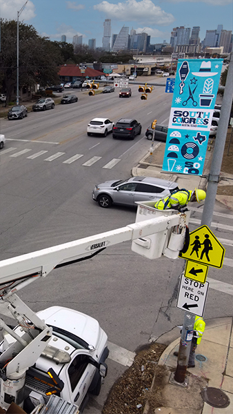 A crew member installs lamppost banners on South Congress Avenue.