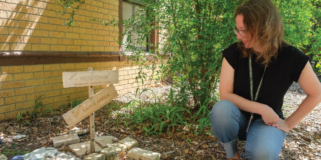 Colleen kneels in the OWL garden to point out designated spots for frogs and toads that are in the shade, have drinking water, and are pesticide-free.
