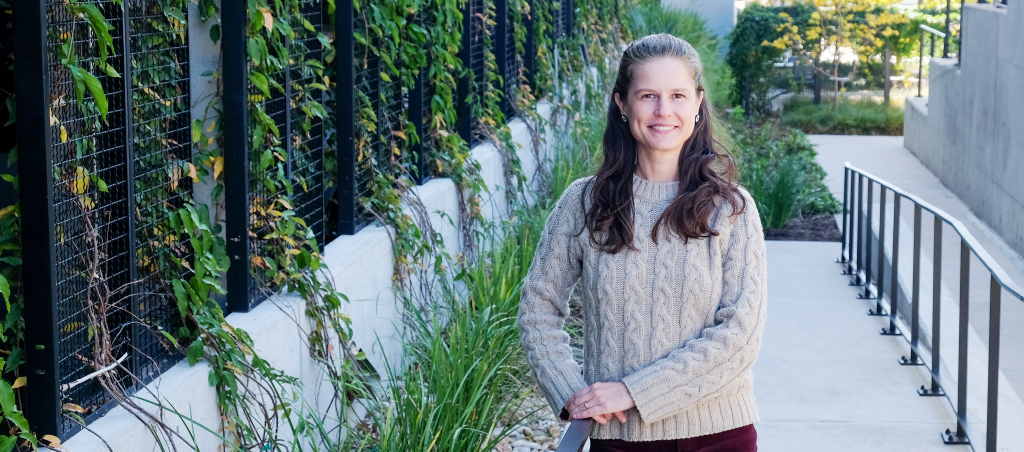 Amanda Mortl leaning against a railing and smiling with lots of green plants around.