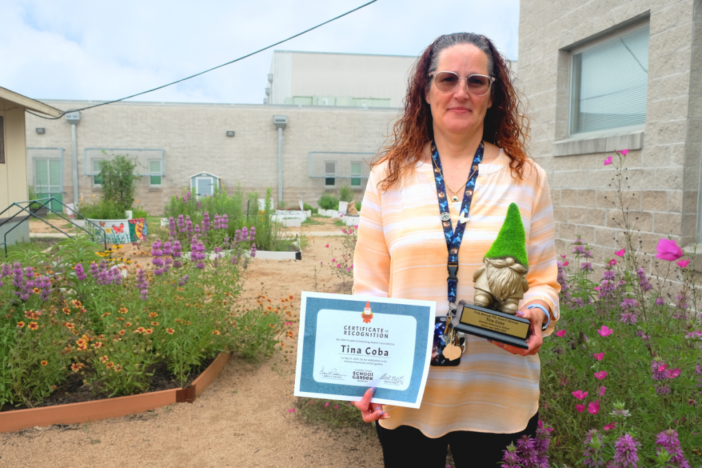 Tina Coba stands in the Overton Elementary School Garden with an award and certificate.