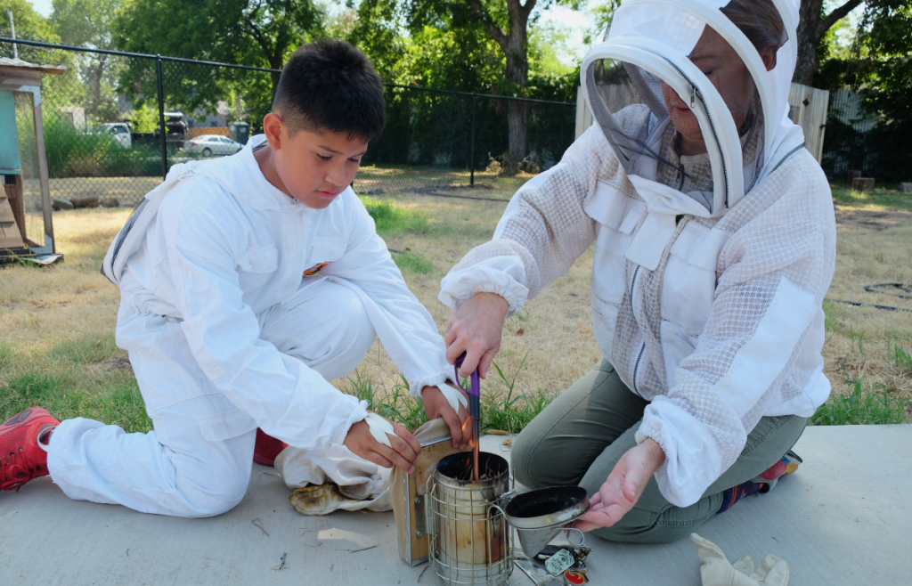 Tadeo helps Stacey light a smoker for the bees.