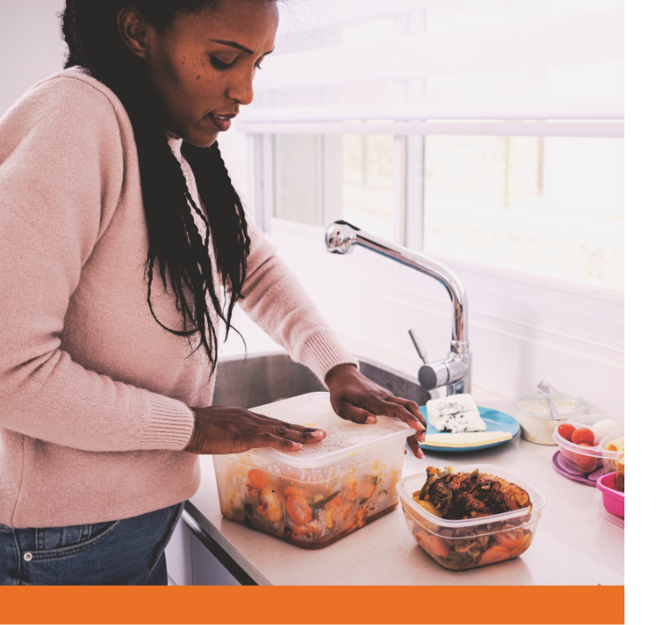 A woman transfers food to a glass Tupperware container.