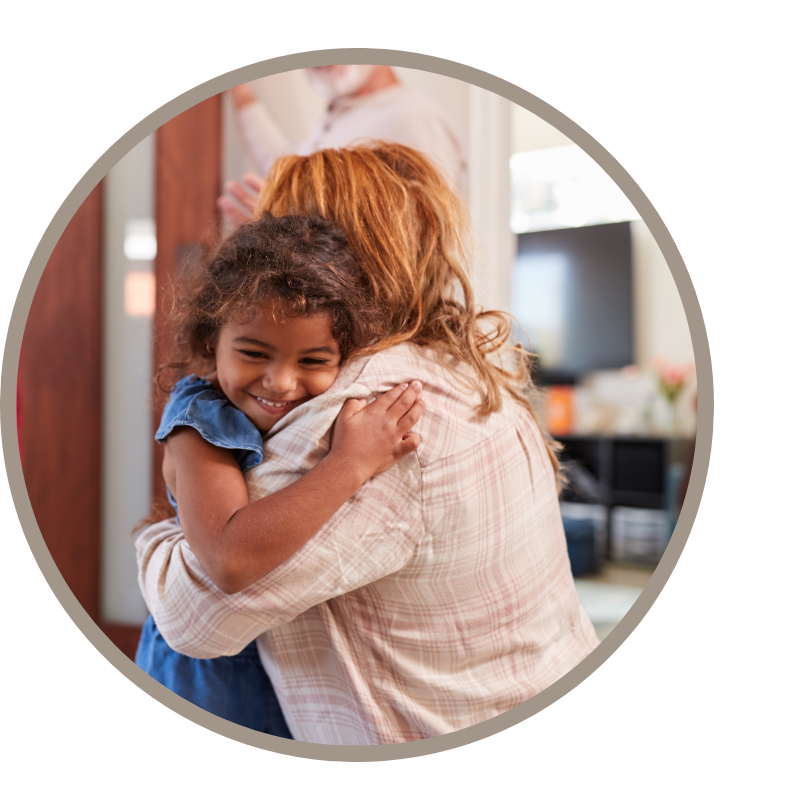 A young girl hugs an older woman inside a front door.