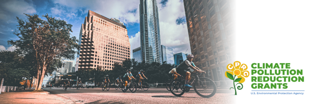 A group of people bike in downtown Austin. A hazy sky is seen in the background. in the bottom right of the photo is the logo for the EPA's Climate Pollution Reduction Grants.