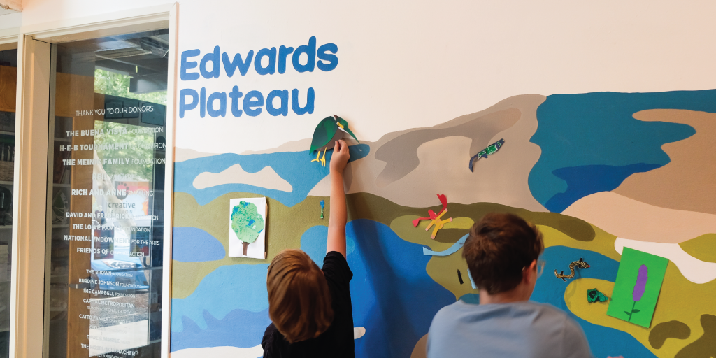 Students placing their native species art pieces on respective ecoregion of the mural