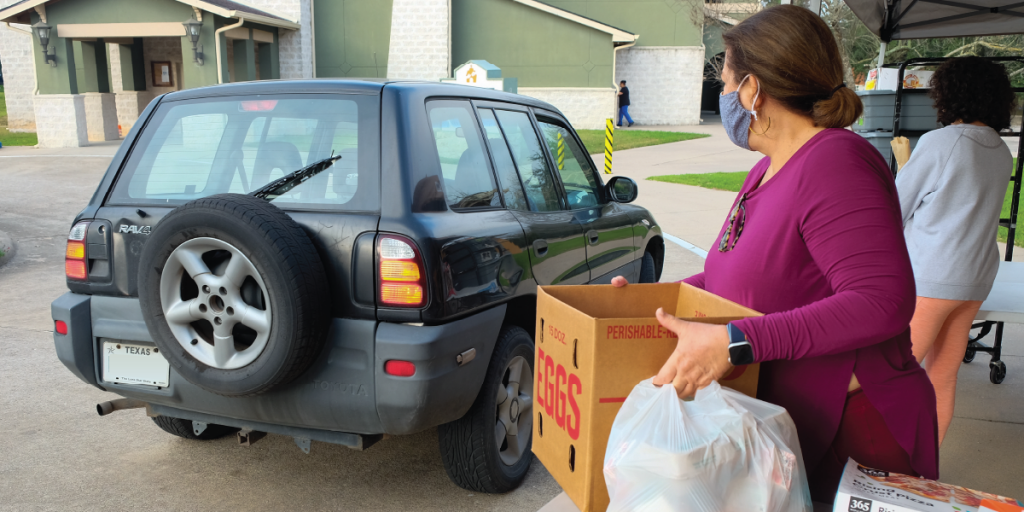 Photo of two women carrying packaged food to a car.