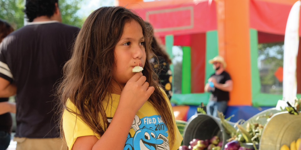 Photo of a young girl sampling food at a pop-up market.