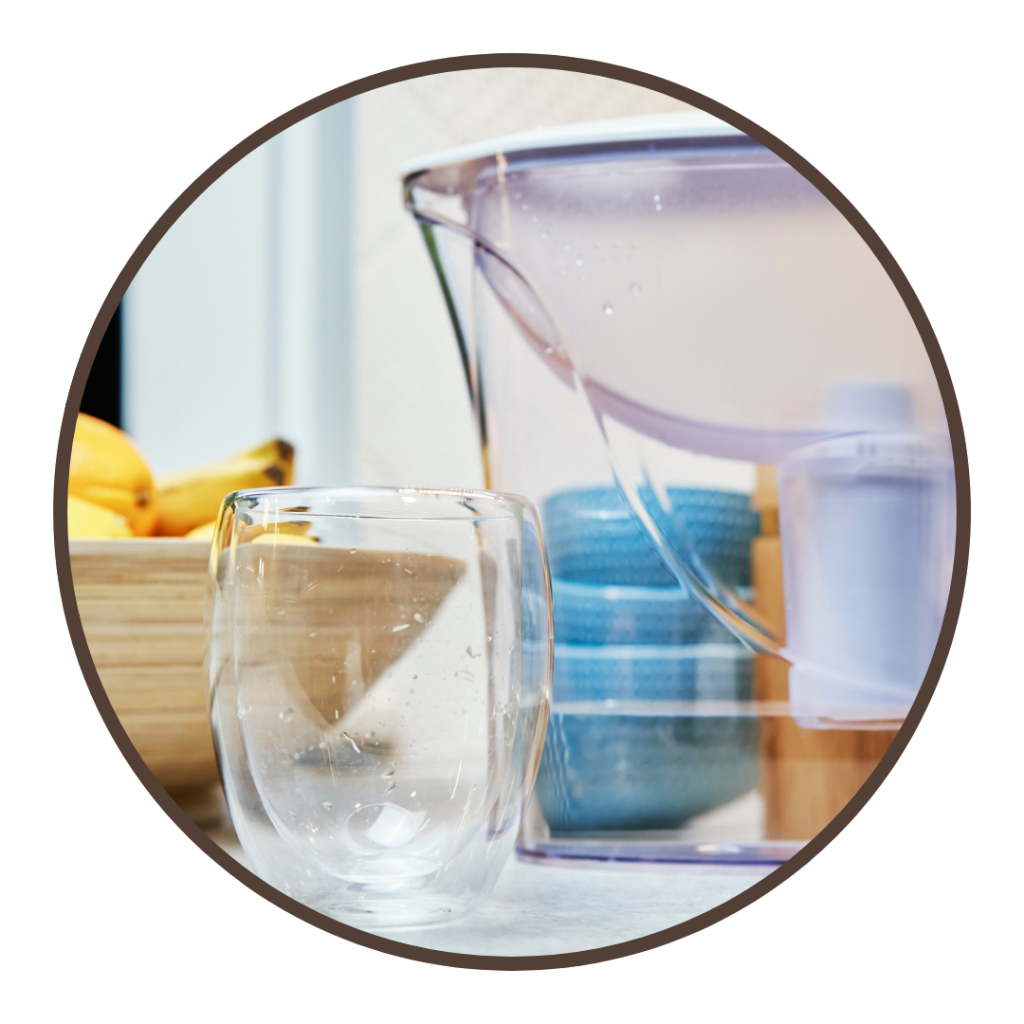 A water pitcher on a counter next to a glass.