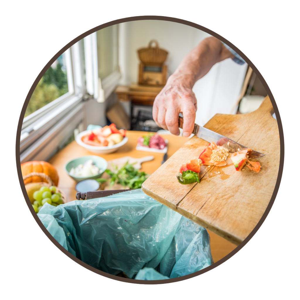 Someone pushes food waste from a cutting board into a countertop composting bin.