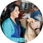 Photo of a woman wearing an apron smiling and giving out a bag of groceries.