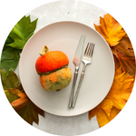 A photo of a ceramic plate with a fork and knife. Fall leaves decorate the table.
