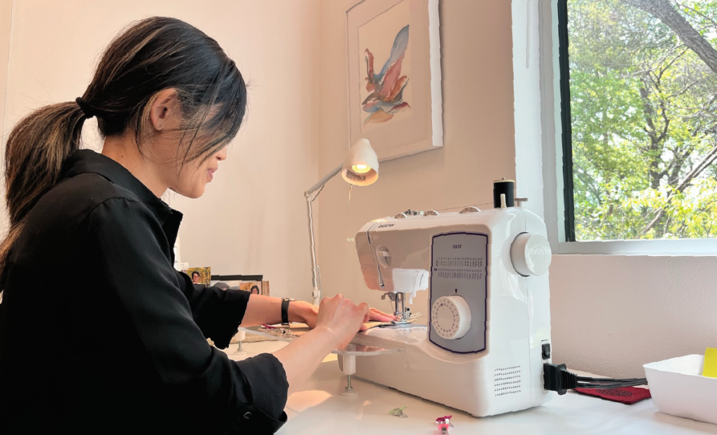 Aileen sits at a sewing machine in her studio. 
