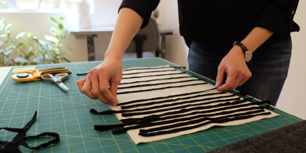 A close up of Aileen's hands laying strips of black fabric over a white rectangle.