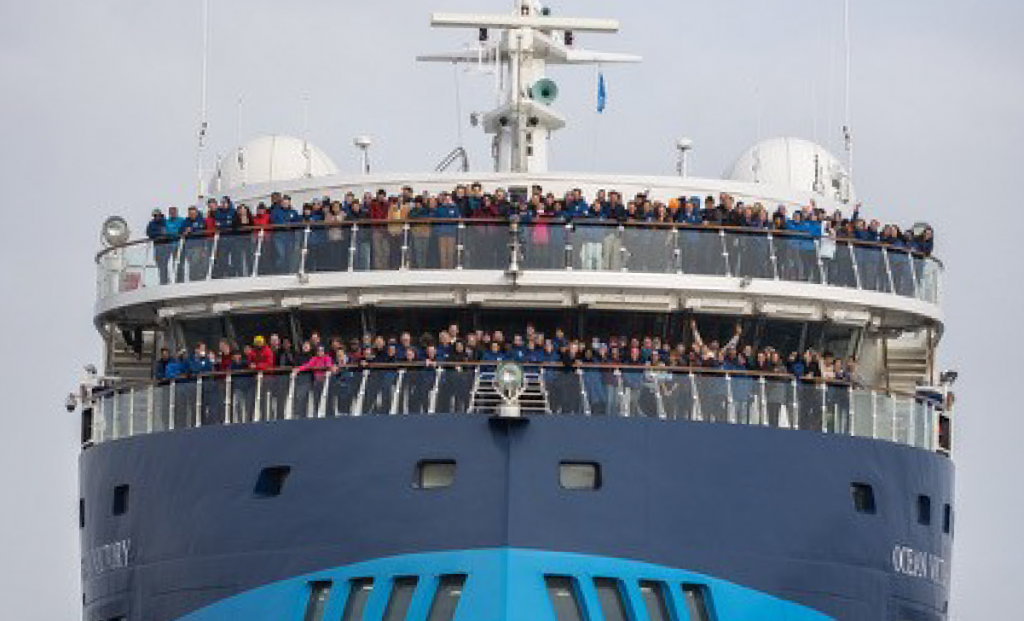 Many people stand on a the deck of a large blue ship.