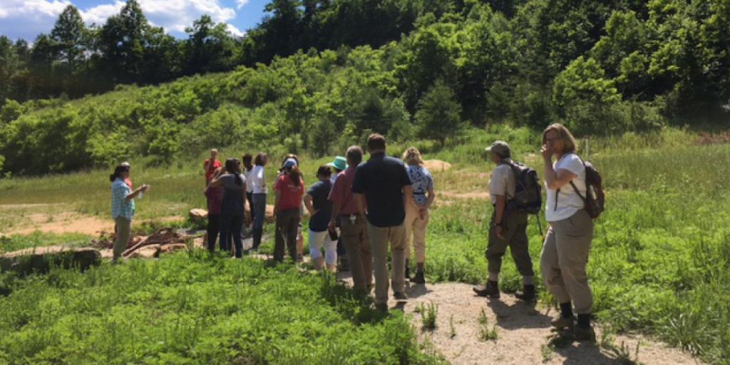 Amy (far left) speaks to a group of hikers along a path.