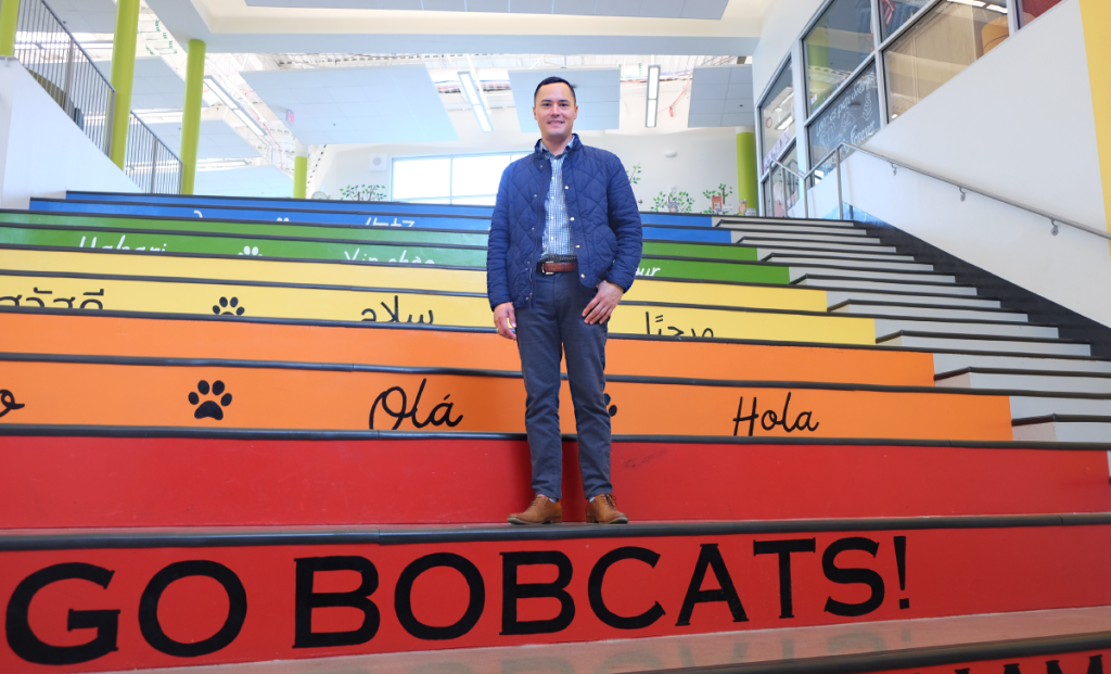 Andrew stands on a rainbow staircase inside T.A. Brown Elementary. The bottom stair reads, "Go bobcats!"