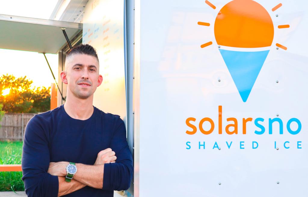 Tom with arms crossed next to solar trailer. 