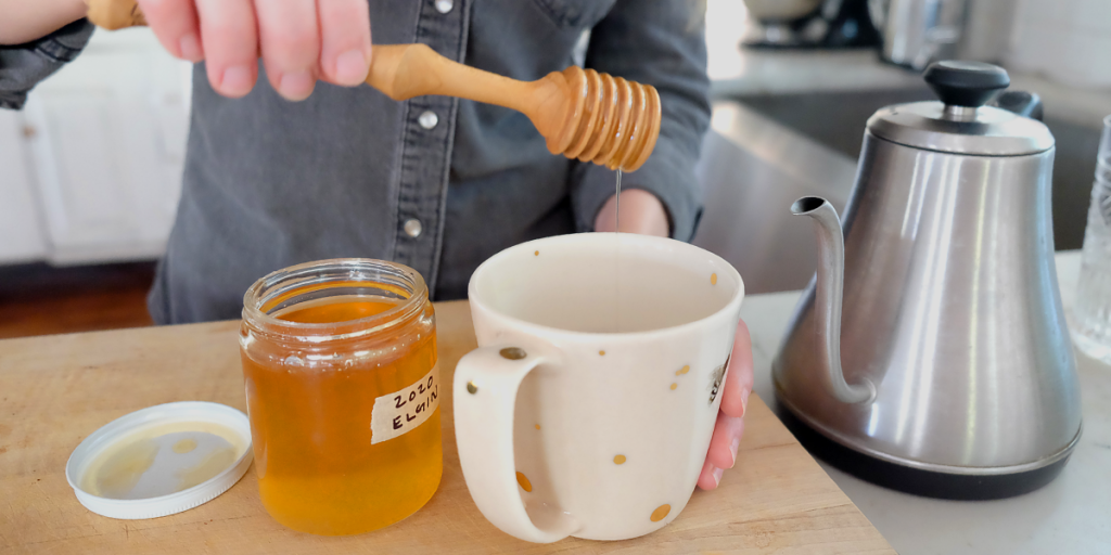 Erika adds honey to a mug using a honey wand.